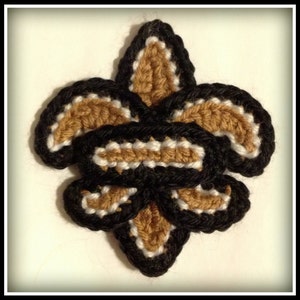Op de afbeelding: Gehaakte fleur-de-lis in zwart, goud en wit garen. De fleur-de-lis is een traditioneel symbool van New Orleans.