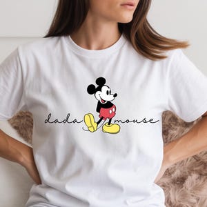 May include: White t-shirt with a Mickey Mouse cartoon design. The graphic shows Mickey in his classic pose, with red shorts, yellow shoes, and black ears. The text "dada mouse" is written in a cursive font.