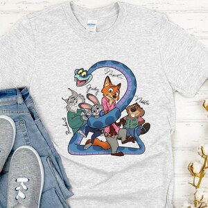 Puede incluir: Una camiseta gris claro con un gr&aacute;fico colorido de personajes de dibujos animados, incluyendo un zorro, un conejo y un castor, con los nombres Judy, Nick y Nibbles. La camiseta se combina con vaqueros azules y zapatillas grises.