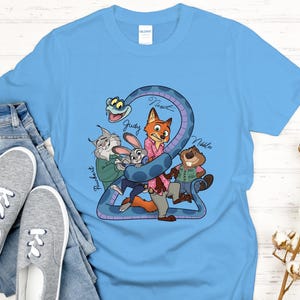 Puede incluir: Camiseta azul claro con un gr&aacute;fico de dibujos animados de personajes de una pel&iacute;cula. El gr&aacute;fico incluye una serpiente, un zorro, un conejo, un castor y un gato. Los nombres de los personajes est&aacute;n escritos en la camiseta. La camiseta se combina con vaqueros azules y zapatillas grises.