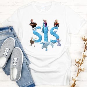 May include: White t-shirt featuring the word "SIS" in blue, with cartoon characters from a popular animated movie. The shirt is paired with blue jeans and gray sneakers.