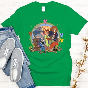 Peut inclure: Un t-shirt vert avec un dessin anim&eacute; des personnages du film Zootopie. Le motif comprend Judy Hopps, Nick Wilde et d'autres personnages, entour&eacute;s de fleurs et d'un arc-en-ciel. Le t-shirt est pr&eacute;sent&eacute; avec un jean bleu et des baskets grises.