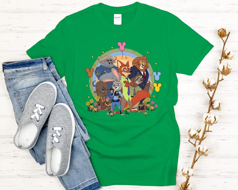 Peut inclure: Un t-shirt vert avec un dessin anim&eacute; des personnages du film Zootopie. Le motif comprend Judy Hopps, Nick Wilde et d'autres personnages, entour&eacute;s de fleurs et d'un arc-en-ciel. Le t-shirt est pr&eacute;sent&eacute; avec un jean bleu et des baskets grises.
