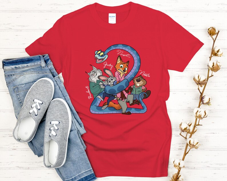 Puede incluir: Camiseta roja con una ilustraci&oacute;n de dibujos animados de personajes animales, incluyendo un zorro, un conejo y un castor, con el texto "2" y nombres de personajes. La camiseta se combina con vaqueros azules y zapatillas grises.