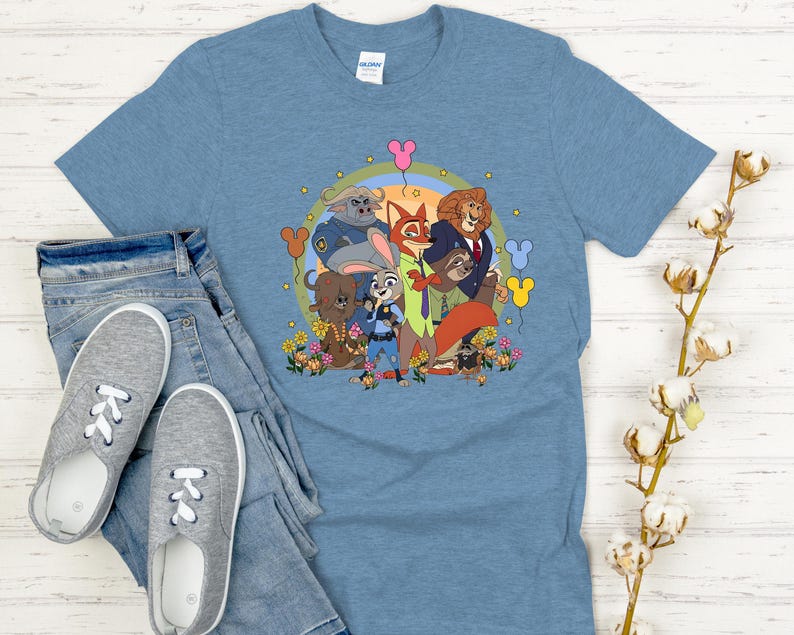 Peut inclure: T-shirt bleu clair avec un motif color&eacute; des personnages du film d'animation Zootopie. Le design comprend Judy Hopps, Nick Wilde et d'autres personnages, entour&eacute;s de fleurs et de ballons. Le t-shirt est associ&eacute; &agrave; un jean bleu et des baskets grises.