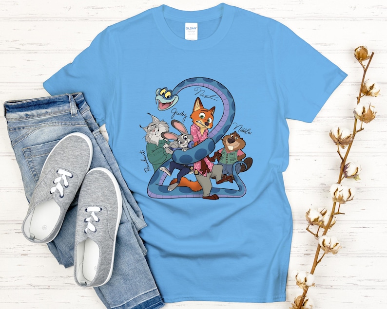 Puede incluir: Camiseta azul claro con un gr&aacute;fico de dibujos animados de personajes de una pel&iacute;cula. El gr&aacute;fico incluye una serpiente, un zorro, un conejo, un castor y un gato. Los nombres de los personajes est&aacute;n escritos en la camiseta. La camiseta se combina con vaqueros azules y zapatillas grises.