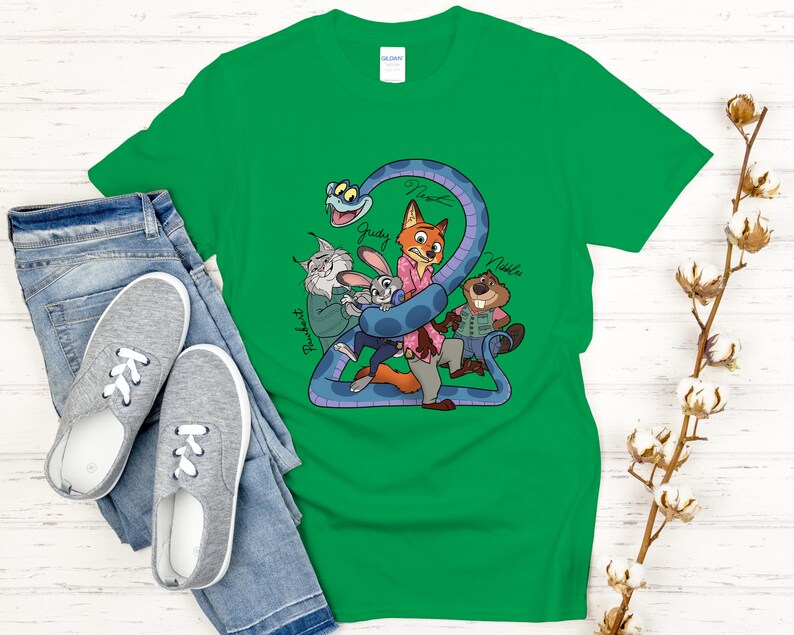 Puede incluir: Camiseta verde con personajes de dibujos animados de Zootopia. El dise&ntilde;o incluye a Judy, Nick y otros personajes, con el n&uacute;mero "2" y los nombres de los personajes. La camiseta se combina con vaqueros azules y zapatillas grises.