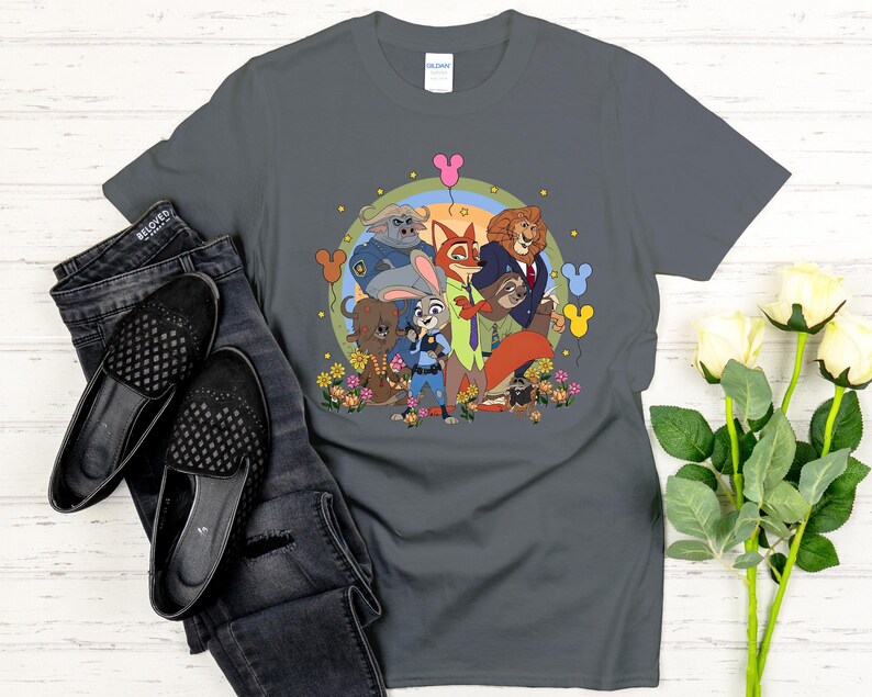 Peut inclure: Un t-shirt gris fonc&eacute; avec une illustration de dessin anim&eacute; color&eacute;e des personnages de Zootopie. Le design comprend Judy Hopps, Nick Wilde et d'autres personnages, entour&eacute;s de fleurs et de ballons. Le t-shirt est associ&eacute; &agrave; un jean et des chaussures noirs.