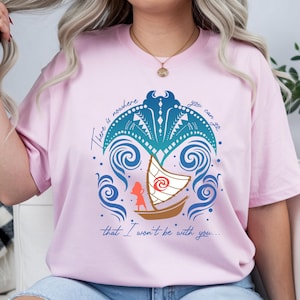 Op de afbeelding: Lichtroze T-shirt met een grafisch ontwerp van een boot, golven en de tekst "There is nowhere you can go that I won't be with you...". Het ontwerp bevat blauwe, turquoise en bruine elementen.