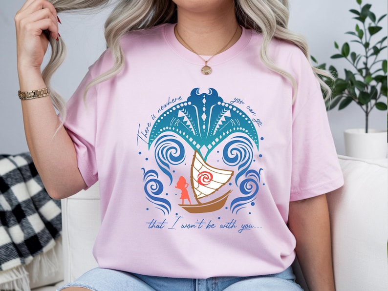 Op de afbeelding: Lichtroze T-shirt met een grafisch ontwerp van een boot, golven en de tekst "There is nowhere you can go that I won't be with you...". Het ontwerp bevat blauwe, turquoise en bruine elementen.