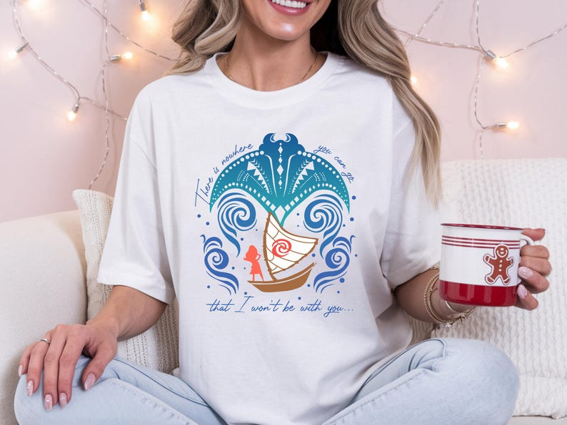 Op de afbeelding: Wit T-shirt met een kleurrijke afbeelding van een boot, golven en de tekst "There is nowhere you can go that I won't be with you...". Een rood-witte mok met een peperkoekmannetje wordt in de hand gehouden.