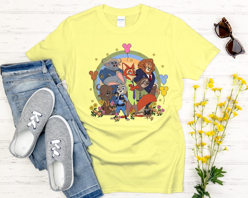 Peut inclure: Un t-shirt jaune clair avec une illustration de personnages de Zootopie. Le design comprend Judy Hopps, Nick Wilde et d'autres personnages, entour&eacute;s de fleurs et de ballons. Le t-shirt est associ&eacute; &agrave; un jean bleu et des baskets grises.