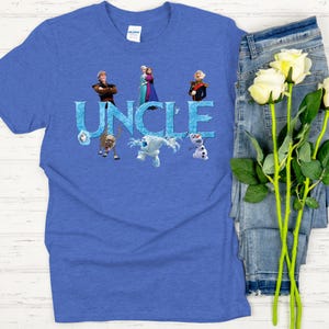 May include: Blue t-shirt with the word "UNCLE" in icy blue letters, featuring characters from the movie Frozen. The shirt has a crew neck and short sleeves. The design includes images of Anna, Elsa, Kristoff, Olaf, and Sven.