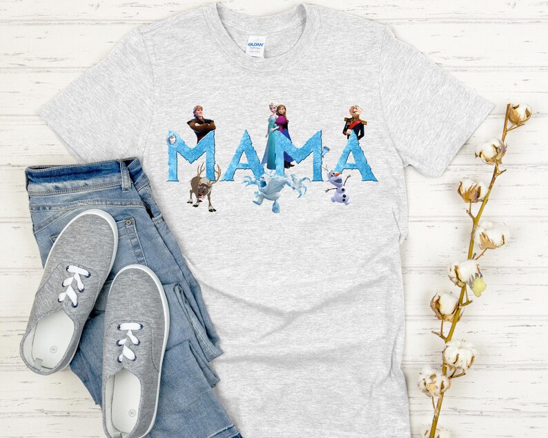 May include: A light gray t-shirt with the word "MAMA" in blue letters, featuring characters from the movie Frozen. The shirt is paired with blue jeans and gray sneakers. The shirt is made of a soft material.