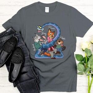 Puede incluir: Una camiseta gris oscuro con una ilustraci&oacute;n de dibujos animados de personajes de Zootopia. El dise&ntilde;o muestra una serpiente azul que rodea a Judy Hopps, Nick Wilde y otros personajes. Los nombres de los personajes est&aacute;n escritos en cursiva.