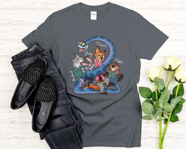 Puede incluir: Una camiseta gris oscuro con una ilustraci&oacute;n de dibujos animados de personajes de Zootopia. El dise&ntilde;o muestra una serpiente azul que rodea a Judy Hopps, Nick Wilde y otros personajes. Los nombres de los personajes est&aacute;n escritos en cursiva.