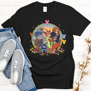 Peut inclure: T-shirt noir avec un motif color&eacute; de personnages de dessins anim&eacute;s, un arc-en-ciel et des fleurs. Le design est pr&eacute;sent&eacute; sur un fond noir. Le t-shirt est associ&eacute; &agrave; un jean bleu et des baskets grises.