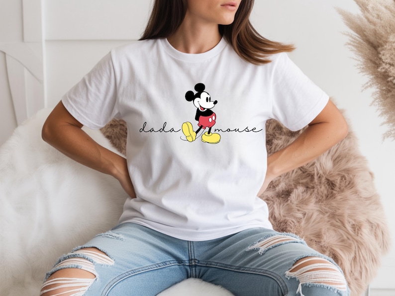 May include: White t-shirt with a Mickey Mouse cartoon design. The graphic shows Mickey in his classic pose, with red shorts, yellow shoes, and black ears. The text "dada mouse" is written in a cursive font.
