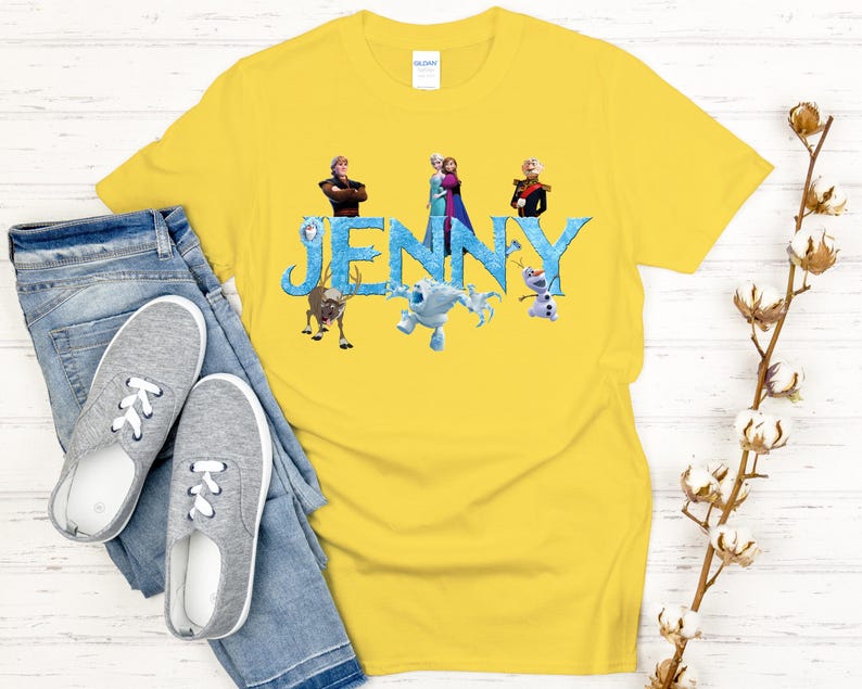 May include: A yellow t-shirt featuring the name "JENNY" in blue letters with characters from a popular animated movie. The shirt is paired with blue jeans and gray sneakers, creating a casual, everyday look.