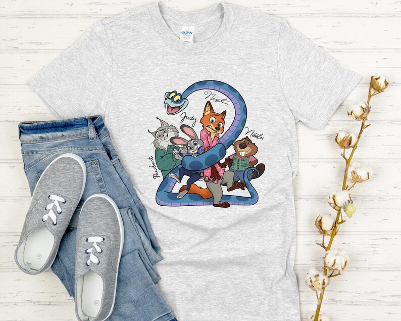Puede incluir: Una camiseta gris claro con un gr&aacute;fico colorido de personajes de dibujos animados, incluyendo un zorro, un conejo y un castor, con los nombres Judy, Nick y Nibbles. La camiseta se combina con vaqueros azules y zapatillas grises.