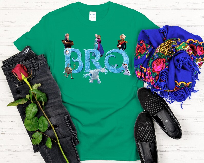 May include: A green t-shirt featuring the word "BRO" in icy blue letters, with characters from the movie Frozen. The shirt is paired with black jeans, a red rose, a blue scarf with floral patterns, and black shoes.