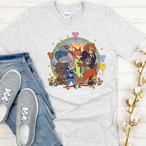 Peut inclure: T-shirt gris clair avec un motif color&eacute; des personnages du film d'animation Zootopie, dont Judy Hopps et Nick Wilde. Le motif est entour&eacute; de fleurs et de ballons. Le t-shirt est pr&eacute;sent&eacute; avec un jean bleu et des baskets grises.