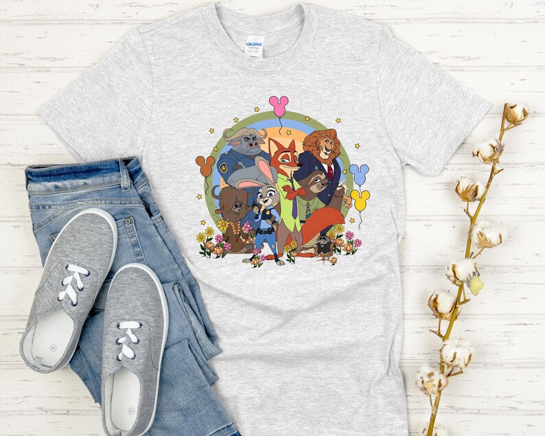 Peut inclure: T-shirt gris clair avec un motif color&eacute; des personnages du film d'animation Zootopie, dont Judy Hopps et Nick Wilde. Le motif est entour&eacute; de fleurs et de ballons. Le t-shirt est pr&eacute;sent&eacute; avec un jean bleu et des baskets grises.