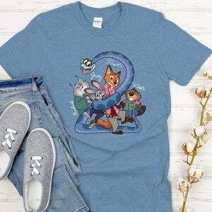 Puede incluir: Una camiseta azul claro con un dibujo animado de personajes de una pel&iacute;cula. El gr&aacute;fico incluye una serpiente y varios personajes de animales, con los nombres Judy, Nick y otros. La camiseta se combina con vaqueros azules y zapatillas grises.