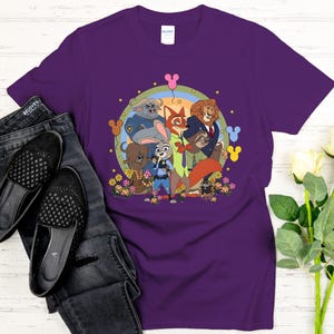 Peut inclure: T-shirt violet avec un motif color&eacute; des personnages du film d'animation Zootopie. Le design comprend Judy Hopps, Nick Wilde et d'autres personnages, entour&eacute;s de fleurs et d'un arc-en-ciel. Le t-shirt est associ&eacute; &agrave; un jean et des chaussures noirs.