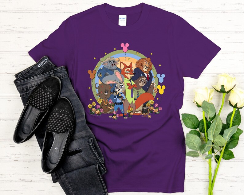Peut inclure: T-shirt violet avec un motif color&eacute; des personnages du film d'animation Zootopie. Le design comprend Judy Hopps, Nick Wilde et d'autres personnages, entour&eacute;s de fleurs et d'un arc-en-ciel. Le t-shirt est associ&eacute; &agrave; un jean et des chaussures noirs.