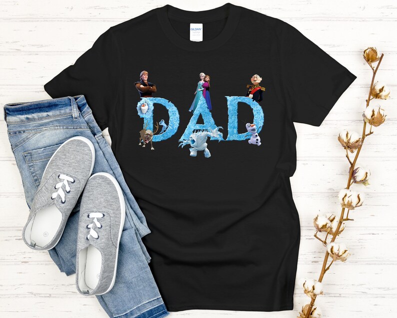 May include: Black t-shirt with the word "DAD" in blue, featuring characters from the movie Frozen. The shirt is paired with blue jeans and gray sneakers. A sprig of cotton adds a decorative touch.