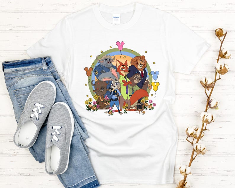 Peut inclure: T-shirt blanc avec une illustration de dessin anim&eacute; color&eacute;e de personnages d'un film d'animation populaire. Le motif comprend un lapin, un renard, un lion et d'autres personnages, entour&eacute;s de fleurs et de ballons. Le t-shirt est pr&eacute;sent&eacute; avec un jean bleu et des baskets grises.