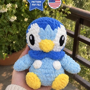 Peut inclure: Un jouet pingouin en crochet pelucheux aux couleurs bleu, blanc et jaune, avec de grands yeux noirs, un bec jaune et des pattes jaunes. Au-dessus, une étoile bleue porte le texte CROCHET PATTERN PDF FILE et une icône de drapeau américain.