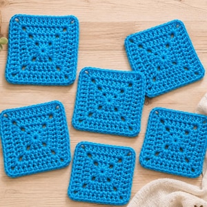 May include: Five square crochet coasters in a vibrant bright blue yarn. Each coaster features a central star-like pattern with openwork stitches radiating outward toward the edges, creating a consistent geometric design across all five pieces.