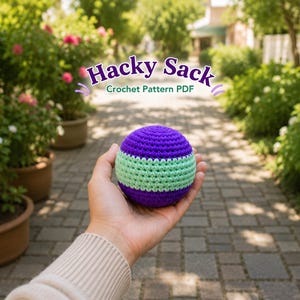 Puede incluir: Un hacky sack de ganchillo esférico con rayas horizontales de hilo morado y verde claro. El texto Hacky Sack Crochet Pattern PDF aparece en letras moradas sobre el objeto, que se sostiene en la palma de una mano.
