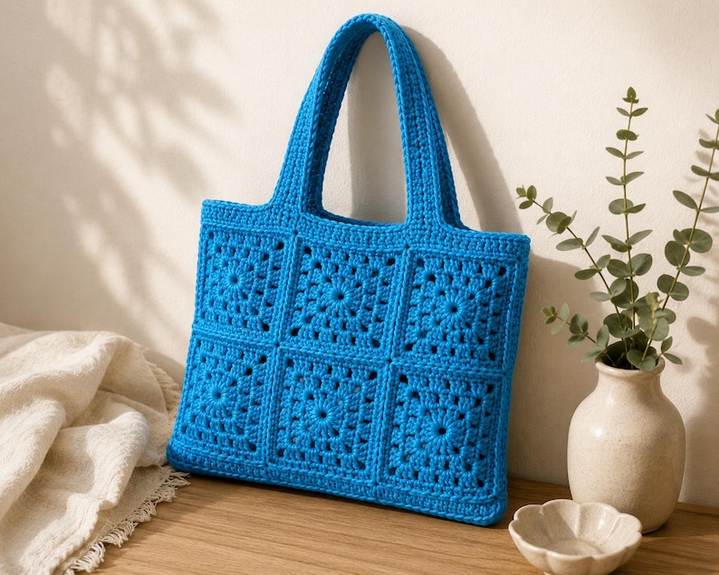 May include: A bright blue tote bag constructed from six square crochet granny motifs arranged in two rows of three. The bag features two matching blue crochet handles and a textured, open-work pattern throughout the entire surface of the bag.