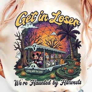 May include: A cream-colored t-shirt featuring a graphic print of cartoon characters on a boat ride. The text reads Get in Loser and We're Haunted by Harvests. The scene includes a geodesic dome, palm trees, bare trees, ghosts, and pumpkins in a dark, spooky setting.