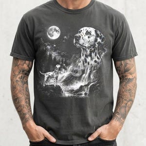 May include: A charcoal grey t-shirt featuring a graphic print of a Dalmatian dog standing near a waterfall, with a larger, ethereal Dalmatian head appearing in the night sky above a full moon, surrounded by a forest and starry night scene.
