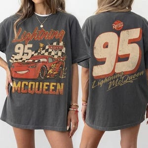 Puede incluir: Camiseta gris oscuro con un dise&ntilde;o de Rayo McQueen de la pel&iacute;cula Cars. El dise&ntilde;o frontal incluye el n&uacute;mero 95, una bandera a cuadros y el nombre McQueen. La parte trasera de la camiseta tambi&eacute;n muestra el n&uacute;mero 95 y el nombre Rayo McQueen.