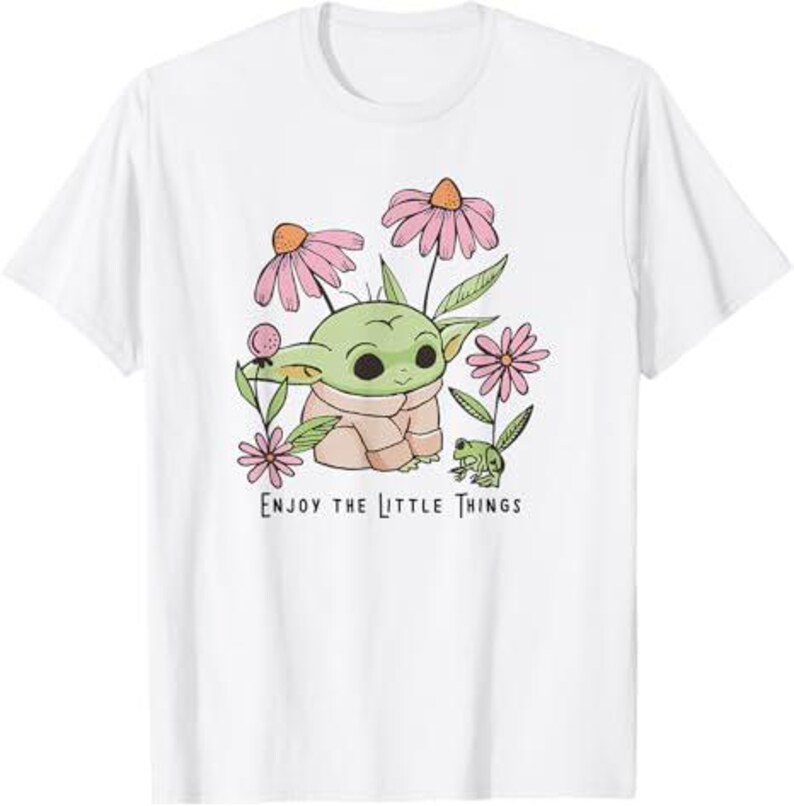 May include: White t-shirt featuring a cartoon character with large eyes, surrounded by pink flowers and green leaves. The text "ENJOY THE LITTLE THINGS" is printed below the character.