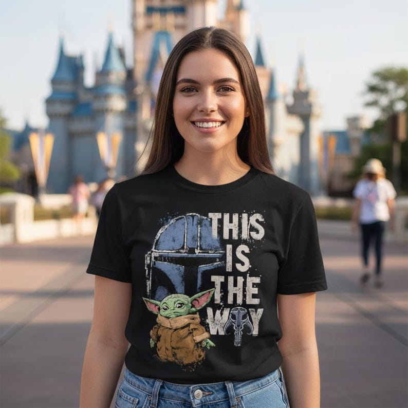 May include: Black t-shirt with a graphic of a helmet, a small green creature, and the phrase "THIS IS THE WAY" in white. The design is inspired by a popular science fiction series.