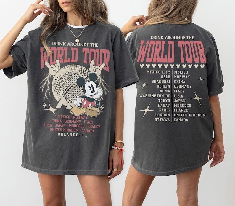 Op de afbeelding: Donkergrijze t-shirt met een afbeelding van Mickey Mouse, een wereldbol en de tekst "DRINK AROUNDE THE WORLD TOUR". Het shirt vermeldt steden als Mexico-Stad, Berlijn en Tokio. De achterkant van het shirt heeft ook de tournaam en steden.