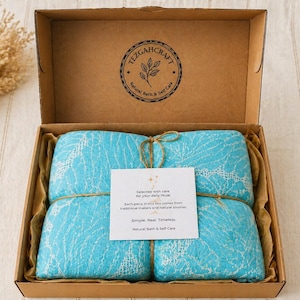 Peut inclure: Une boîte cadeau en carton brun contenant deux textiles bleu vif pliés avec un motif en dentelle blanche. Le couvercle porte un logo circulaire noir TEZGAHCRAFT Natural Bath & Self Care. Une carte blanche avec du texte est attachée aux textiles.