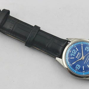 May include: A wristwatch with a blue face and a black leather band. The watch face has white numerals and the text "hmt PILOT PARA SHOCK 17 JEWELS". The band has a silver buckle.