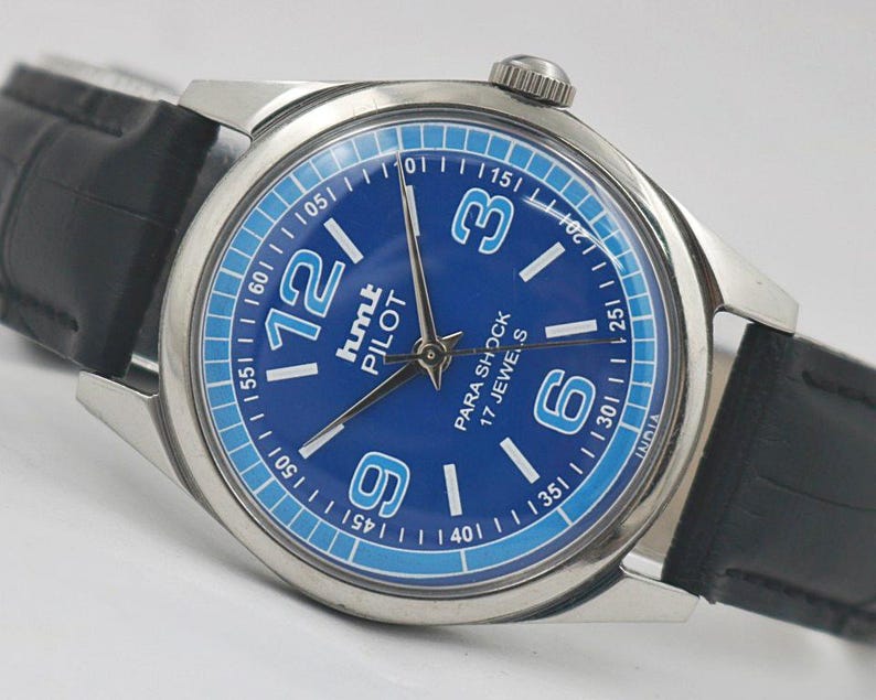May include: A silver-toned wristwatch with a blue face and black leather band. The watch face features large white numerals at the 12, 3, 6, and 9 o'clock positions, with smaller markers around the perimeter. The text "PARA SHOCK 17 JEWELS" is visible.