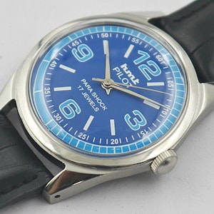 May include: A vintage HMT Pilot watch with a blue dial and silver-tone case. The watch features white numerals, a blue outer ring, and a black leather strap. The dial reads "PARA SHOCK 17 JEWELS".