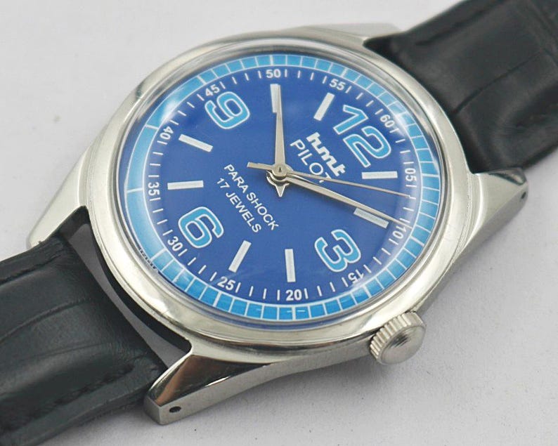 May include: A vintage HMT Pilot watch with a blue dial and silver-tone case. The watch features white numerals, a blue outer ring, and a black leather strap. The dial reads "PARA SHOCK 17 JEWELS".
