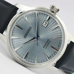 May include: A Seiko Presage Automatic watch with a light blue sunray dial, silver-tone indices, and a date window at the three o'clock position. The watch features a stainless steel case and a black leather strap with a blue second hand.