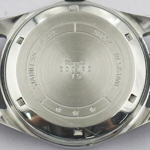 May include: Close-up of the back of a silver-toned wristwatch with a black leather band. The watch face is stainless steel and features the text "STAINLESS STEEL", "SHOCK RESISTANT", and "200182 TS".