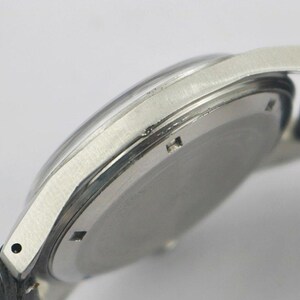 May include: Close-up of a silver-toned wristwatch with a black leather strap. The watch has a clear, domed crystal and a circular face. The watch band is attached to the watch case with small, silver-toned lugs.